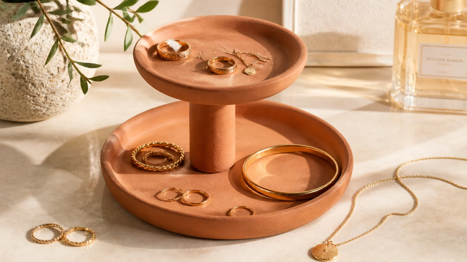 A two-tier clay stand with a small dish stacked above a larger one on a central post, holding rings and bracelets.