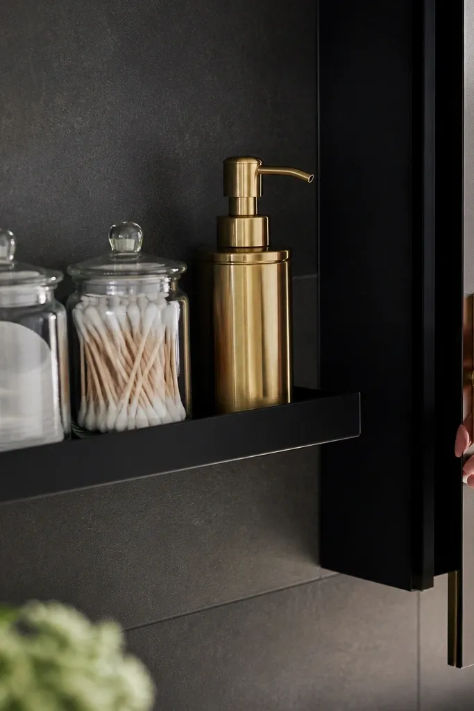 Two matte black floating shelves with brass pump bottles and matching glass jars
