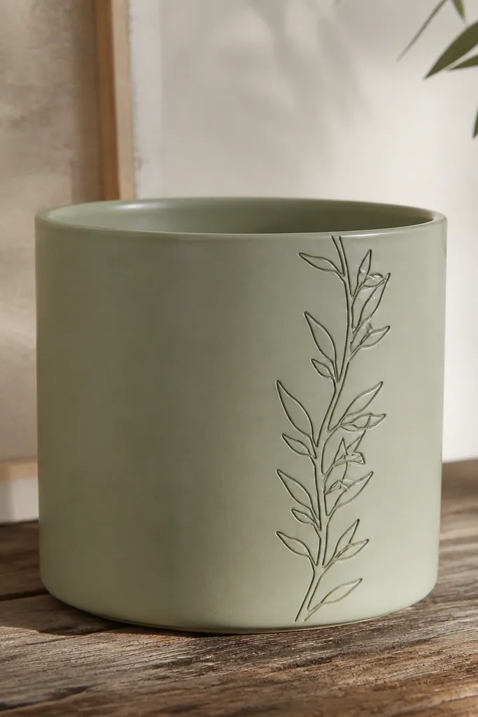 A light sage pot with a narrow vertical strip of black botanical line drawings (simple stem and leaves) on one side.