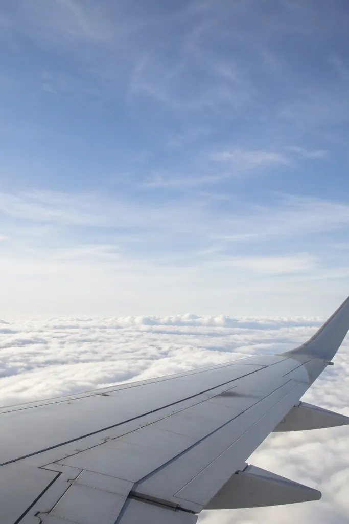 Airplane window view with wing and clouds in bright daylight