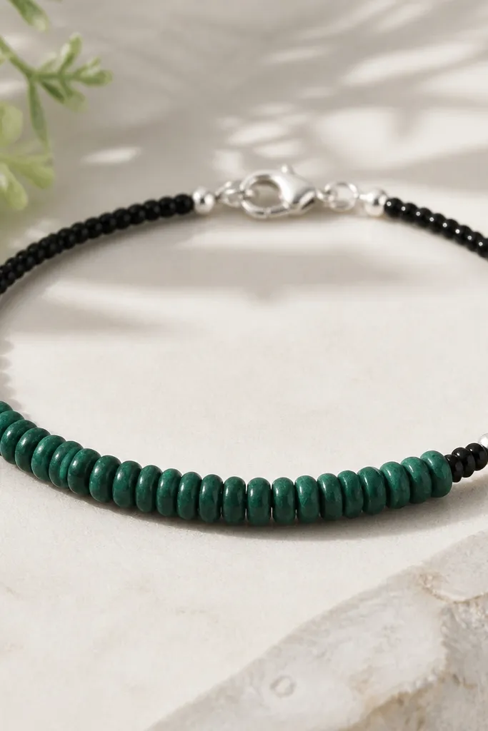 A bracelet with emerald green clay beads in the center and black micro seed beads forming a thin border between bead groups. The metal is silver, and the clasp is a simple silver lobster clasp.