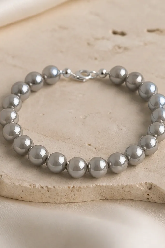 A bracelet made of pearl gray clay beads that look mirror-like. The beads are uniform size, and there are almost invisible clear spacers between them. The metal is minimal silver.