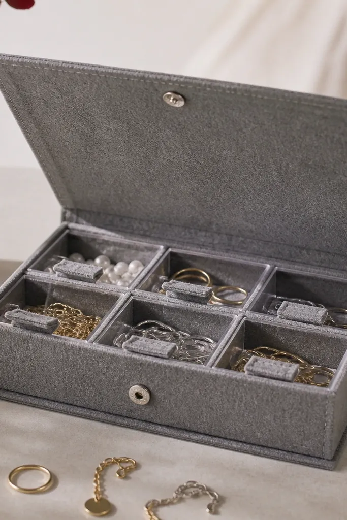 A rectangular felt board in gray with a snap closure lid. Under the lid are small drawer-like compartments made from felt and thin plastic, each holding a different jewelry category.