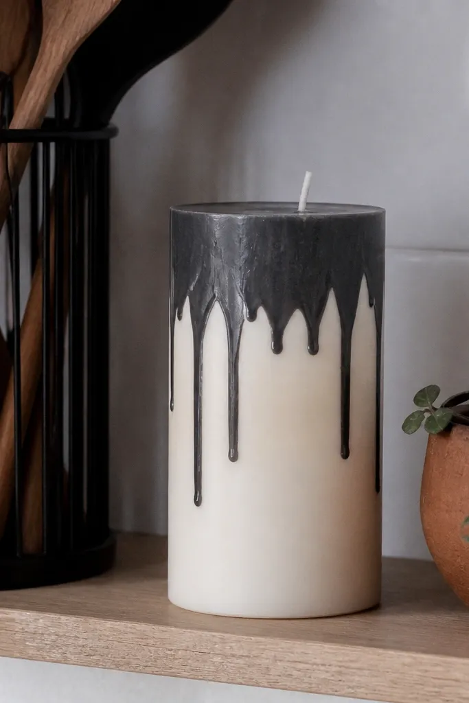 A deep black drip pattern at the top edge of an off-white candle