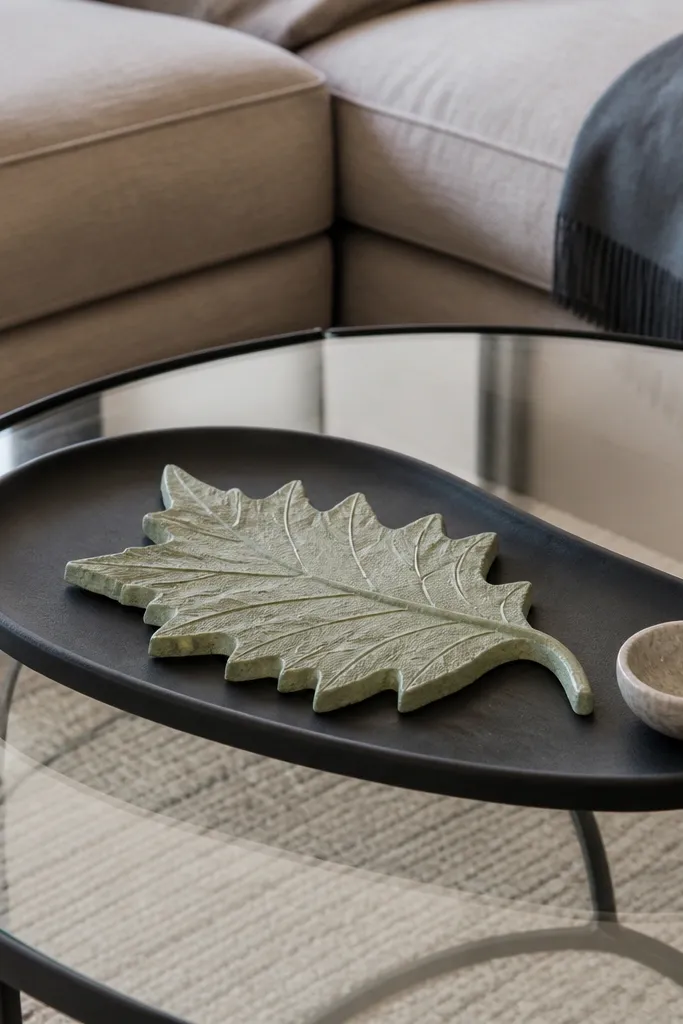 Asymmetrical tray with one oversized leaf sculpture on glass table