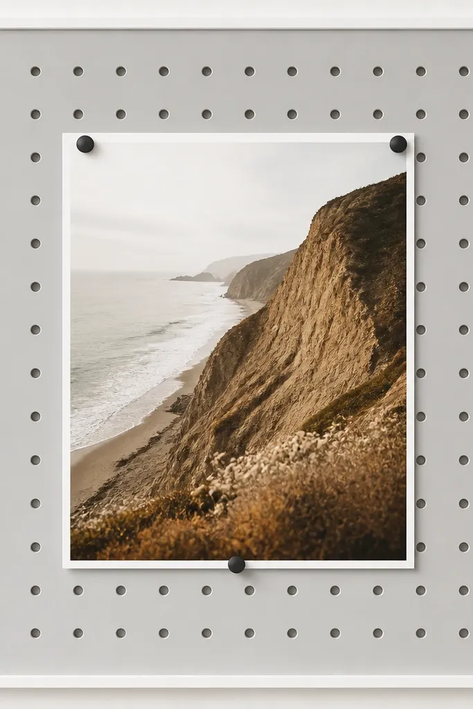 A pegboard backing painted light gray. A photo sits centered, held by two or three small black pins. A thin white border surrounds the pegboard window, keeping the look clean.