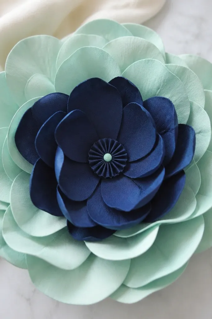 A large flower with outer petals in mint and inner petals in navy. The center is a tiny navy button-like rosette with a small mint dot.