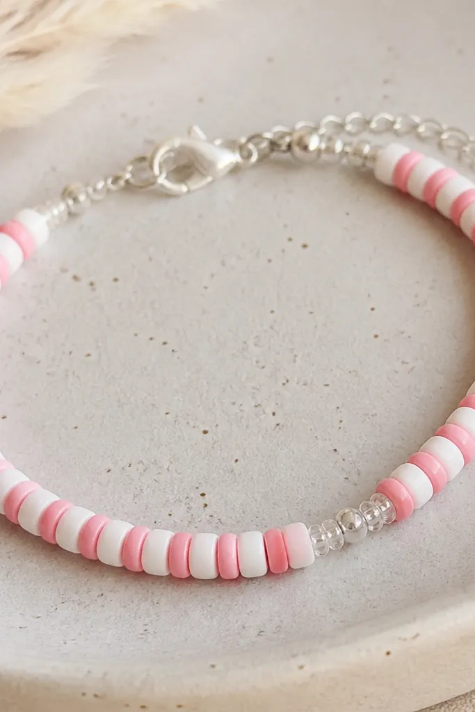 A close-up of a bracelet where pink and white clay beads alternate in a tight row. Tiny clear seed beads pinch at two points near the clasp, creating a delicate sparkle line.