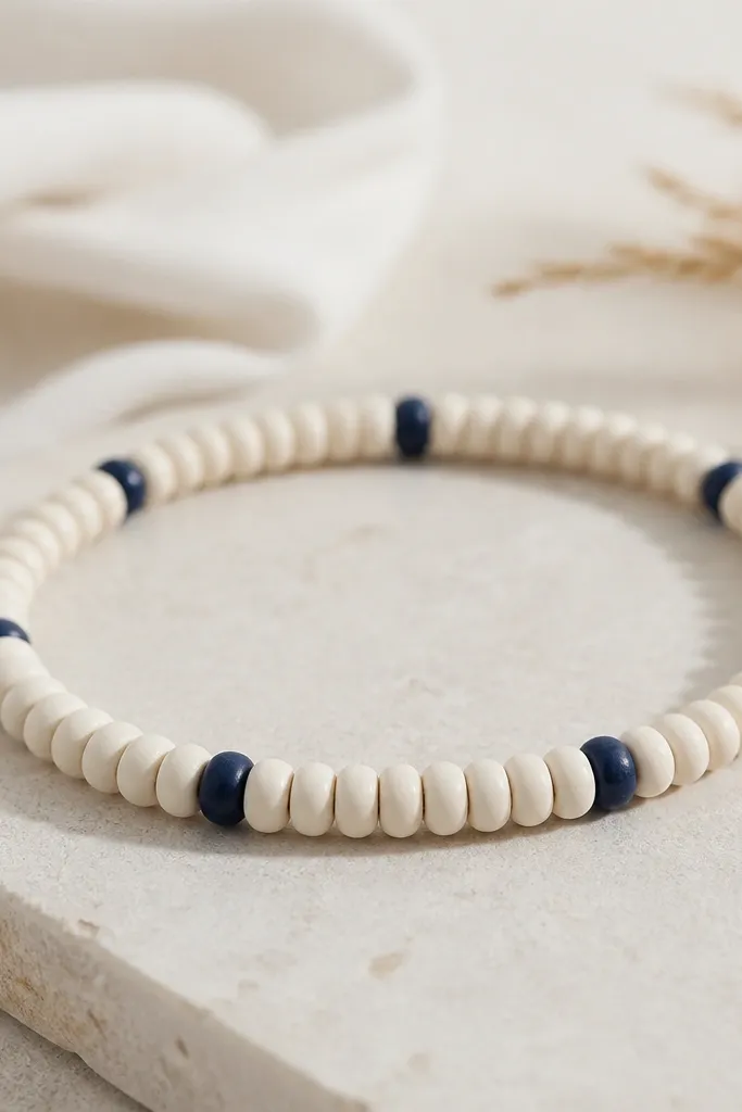 A bracelet with mostly cream clay beads and a few navy accent beads shaped like letter-like dots. The navy pieces repeat every few beads for a subtle pattern.
