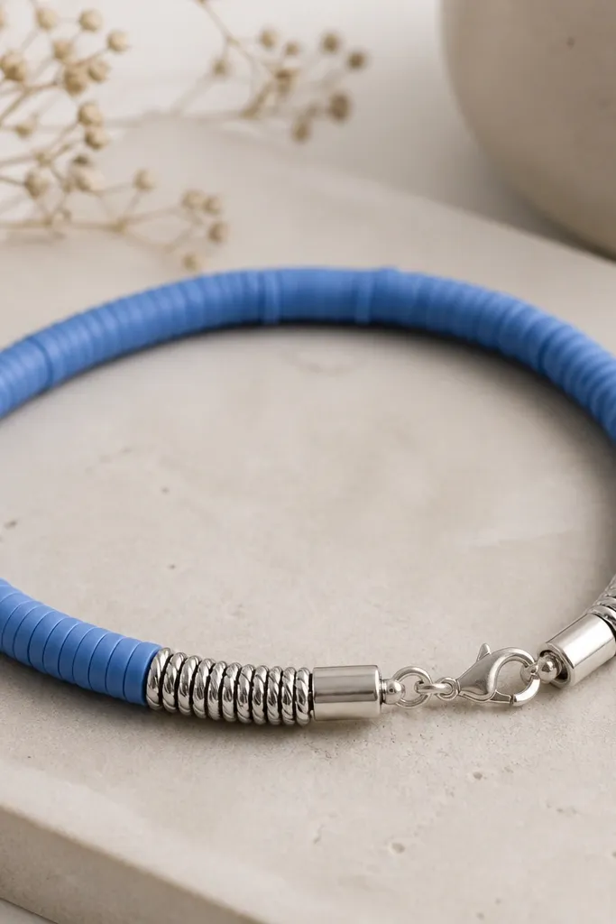A bracelet of cornflower blue clay beads with a silver-toned end section that looks like crimped wire. The clasp area has clean metal caps.