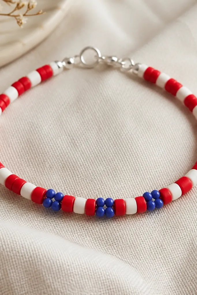 A bracelet with red and white clay beads alternating, plus tiny blue clusters (small round clay beads) grouped near the center. The clasp is simple and silver.