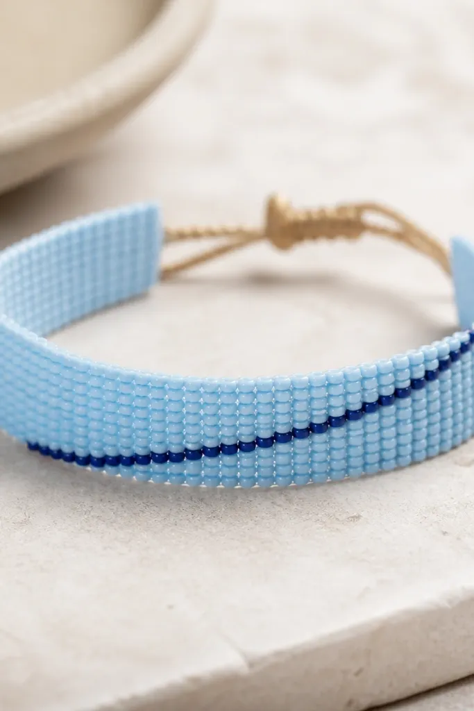 A sky blue bead bracelet where a thin diagonal stripe of navy seed beads runs across the bracelet length. The stripe is crisp and straight.