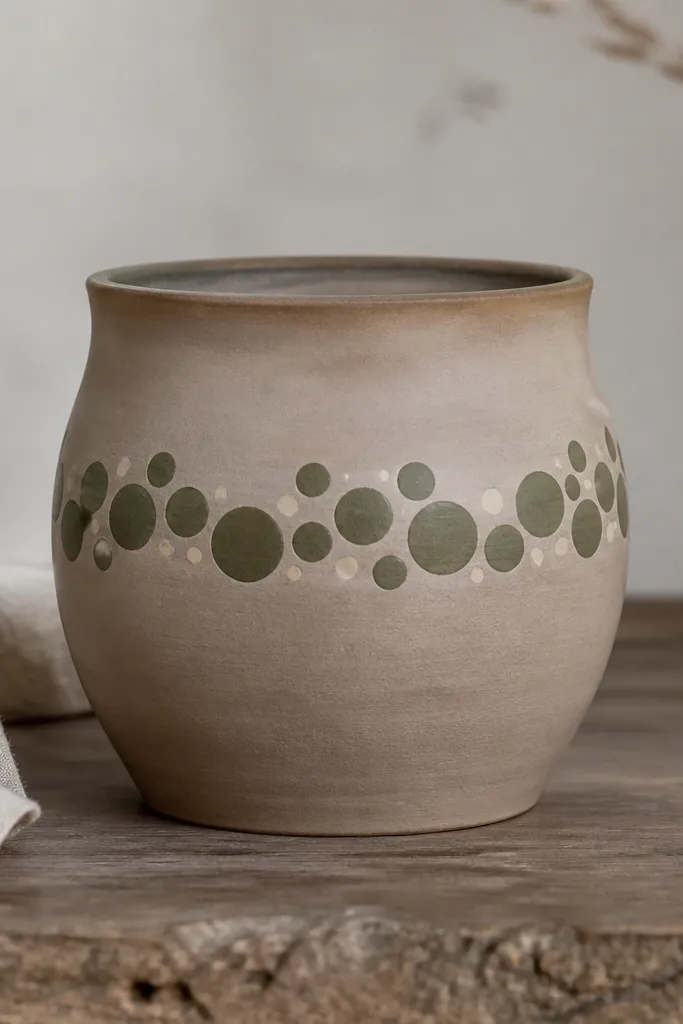 A medium pot with a muted clay base, one horizontal band of olive dots in different sizes, and tiny cream highlights between clusters.