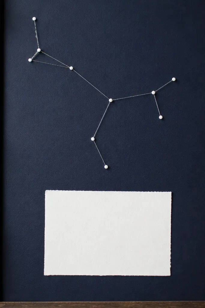 A navy board with tiny white dot stickers. Thin silver thread lines connect the dots into a constellation shape. A small scripture card sits in the bottom third.