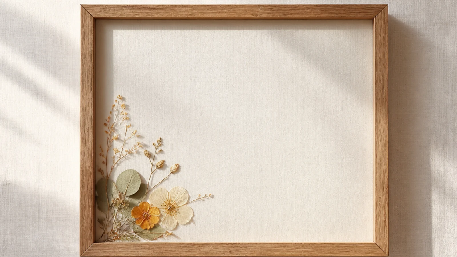 A frame with a small pressed arrangement placed low in one corner, leaving most of the white backing empty.