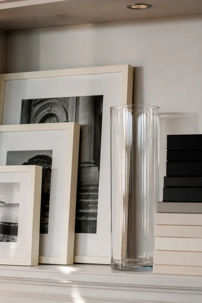 Cream and black framed photos with stacked books and a tall clear glass vase