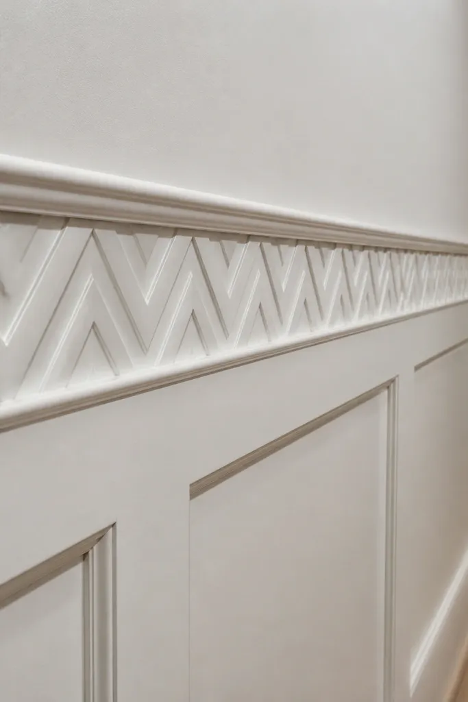 Wainscoting with a chevron trim border along the top rail on a staircase wall
