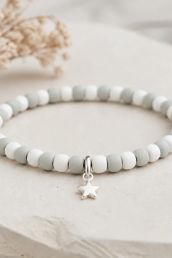 A delicate bracelet with small 6mm clay beads in pale gray and white. At the center front, a tiny star charm hangs from a silver jump ring, with the rest of the bracelet staying simple.