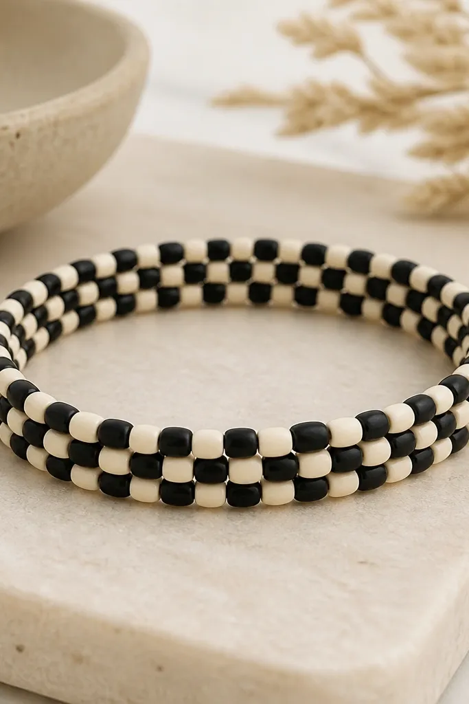 A bracelet that looks like a checkerboard. Clay beads alternate between matte black and matte cream in a tight grid-like sequence, with no spacers.