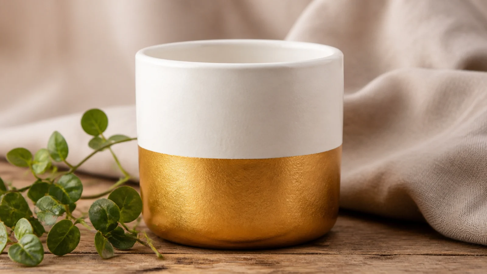 A small white pot with the bottom quarter painted in shimmering gold in a clean level line, top left white.