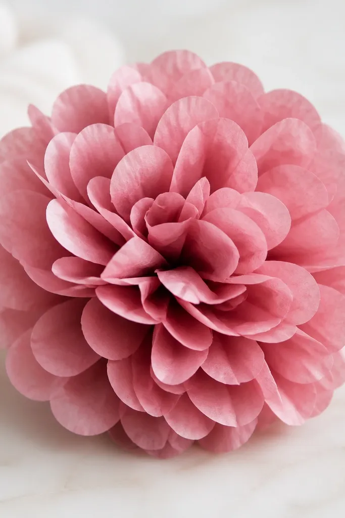 A compact peony pom made from layered tissue fans, about 8 inches wide, in dusty rose. The petals are round and clustered tightly.