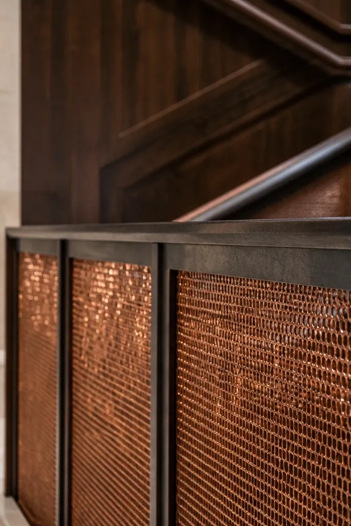 Hammered copper mesh panels between black steel posts on a spiral stair