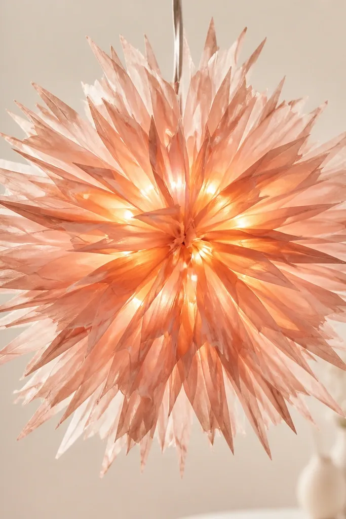 A starburst flower made of rose-gold tissue strips radiating outward, with LEDs placed in the center so the glow spreads through each strip.