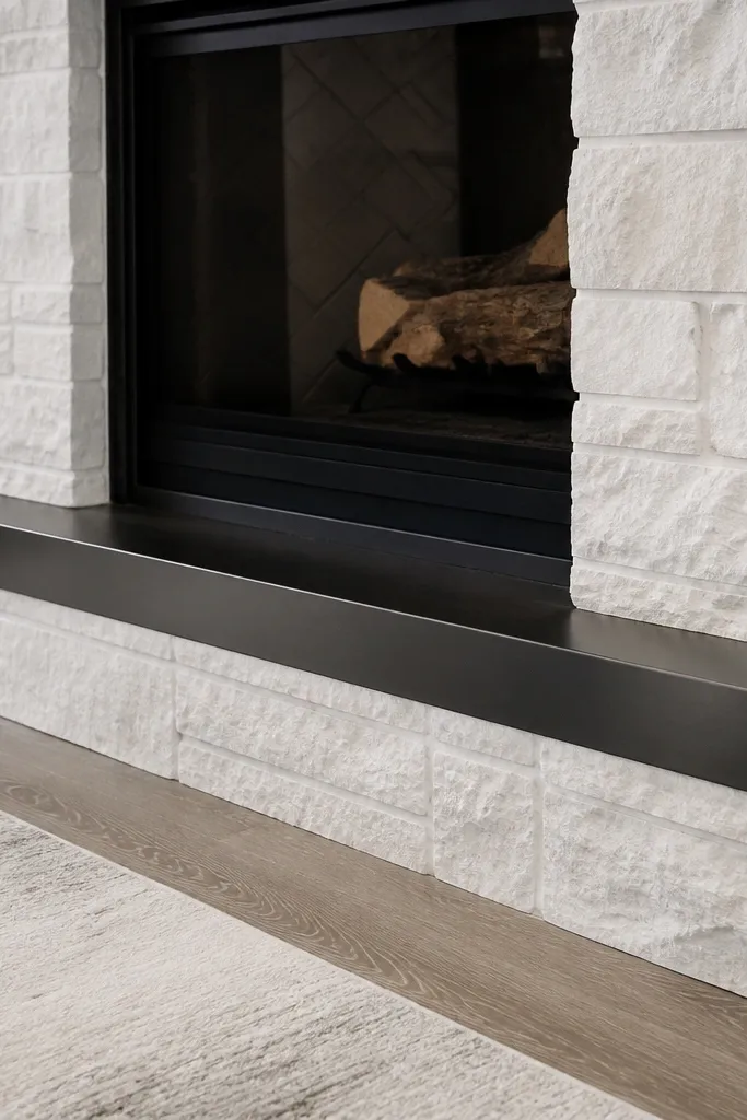 White stone fireplace with stone hearth apron and matte metal kick plate
