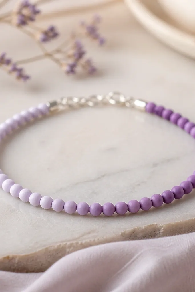 A delicate lilac ombre bracelet made with tiny 4mm clay beads in a smooth gradient from pale lilac to deeper purple; silver crimp beads visible near the ends.