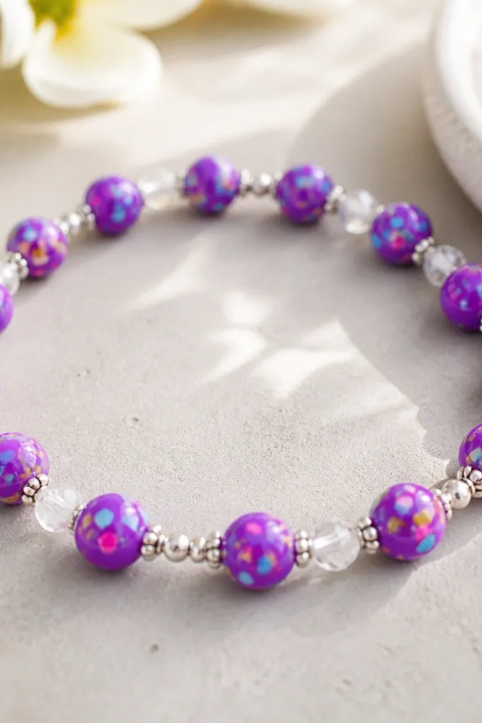 A bright purple bracelet with small confetti-speckled clay beads mixed with tiny silver micro spacer beads and a few clear round spacers; it looks sparkly and fun.