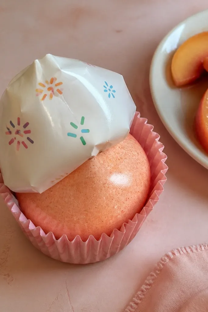 Peach cupcake with white frosting and small sprinkle dots on top